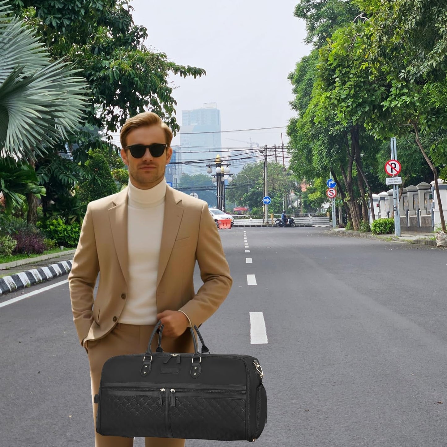 Man in a suit holding a black bag on a city street with trees and buildings in the background.