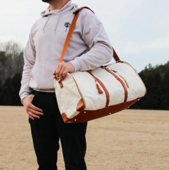 Person holding a white duffel bag with brown accents outdoors