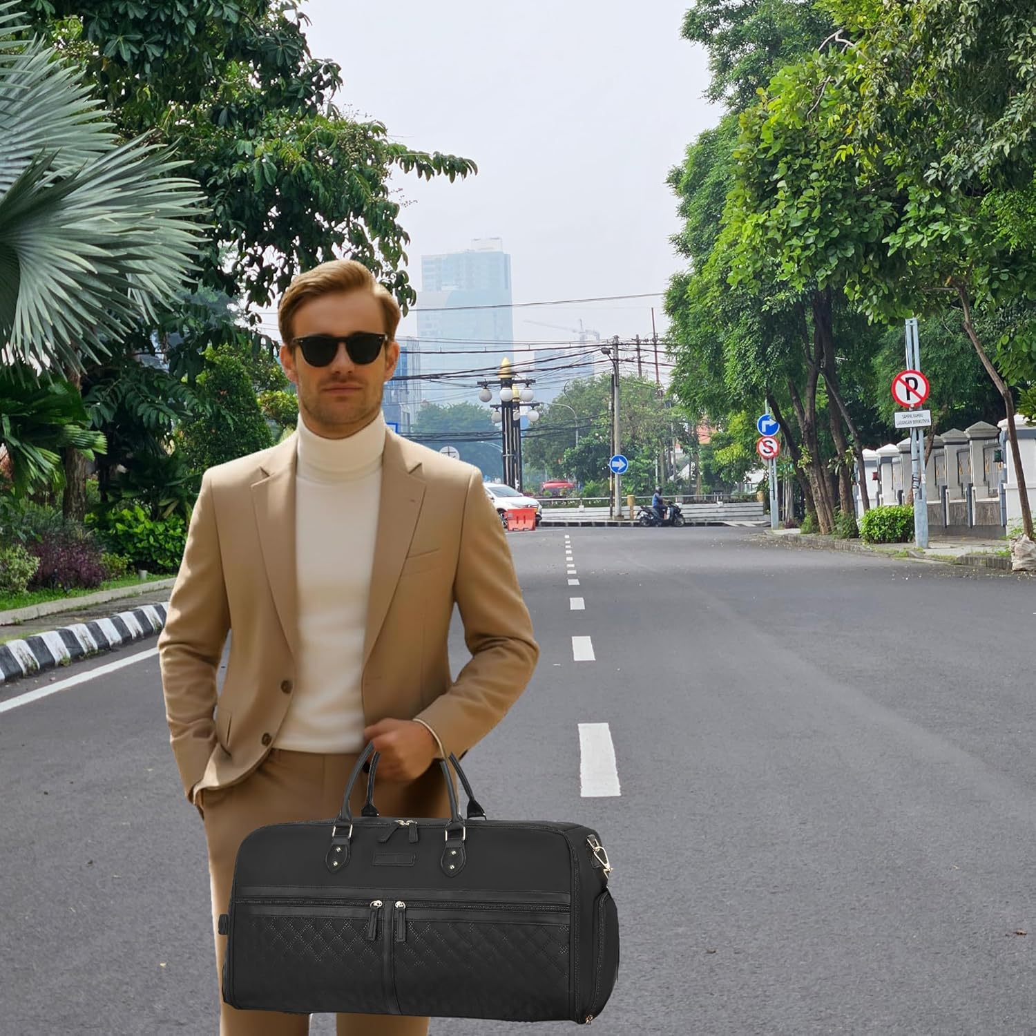 Man in a suit holding a black bag on a city street with trees and buildings in the background.